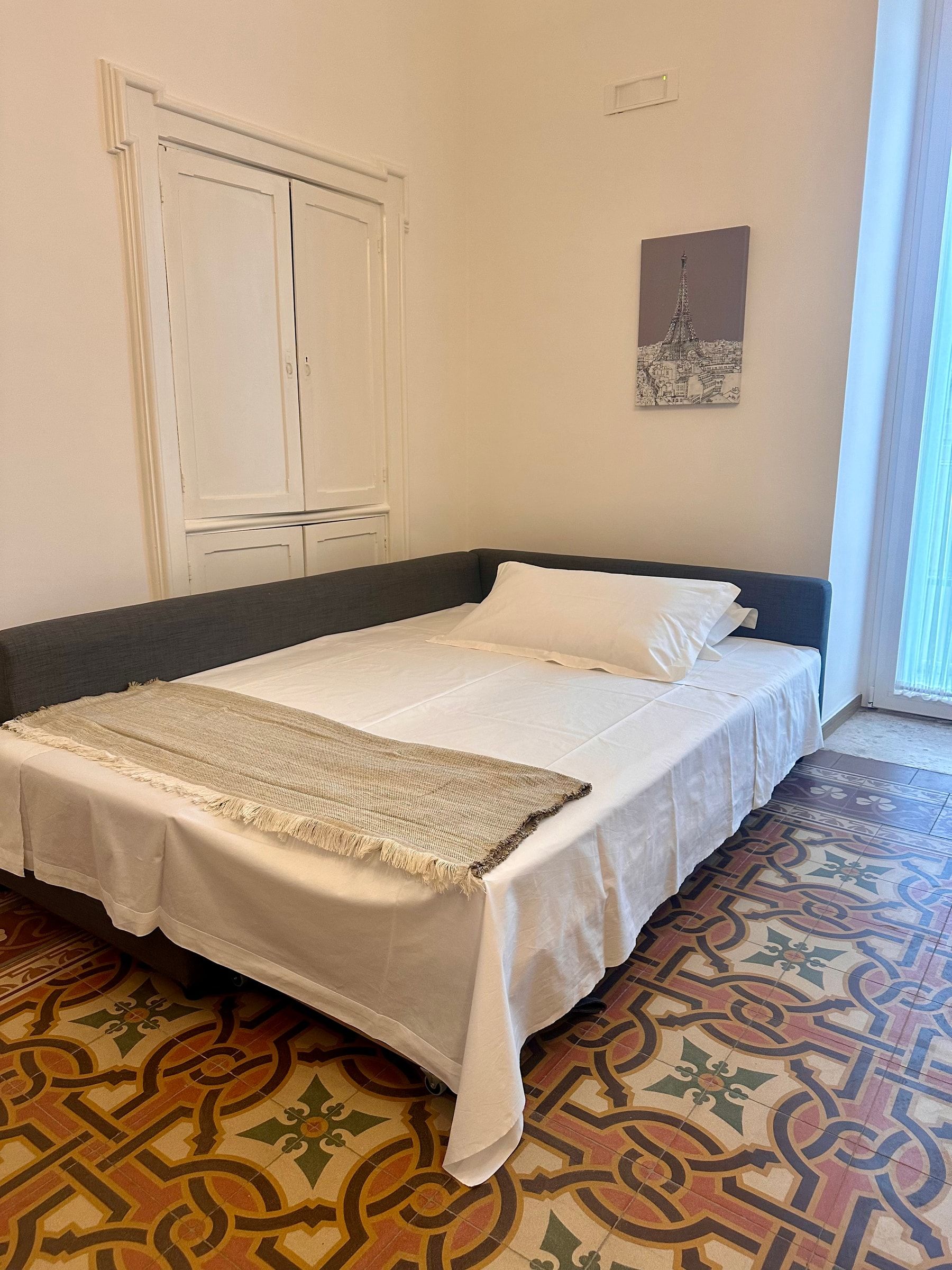 Il divano del soggiorno aperto come letto matrimoniale, con lenzuola bianche