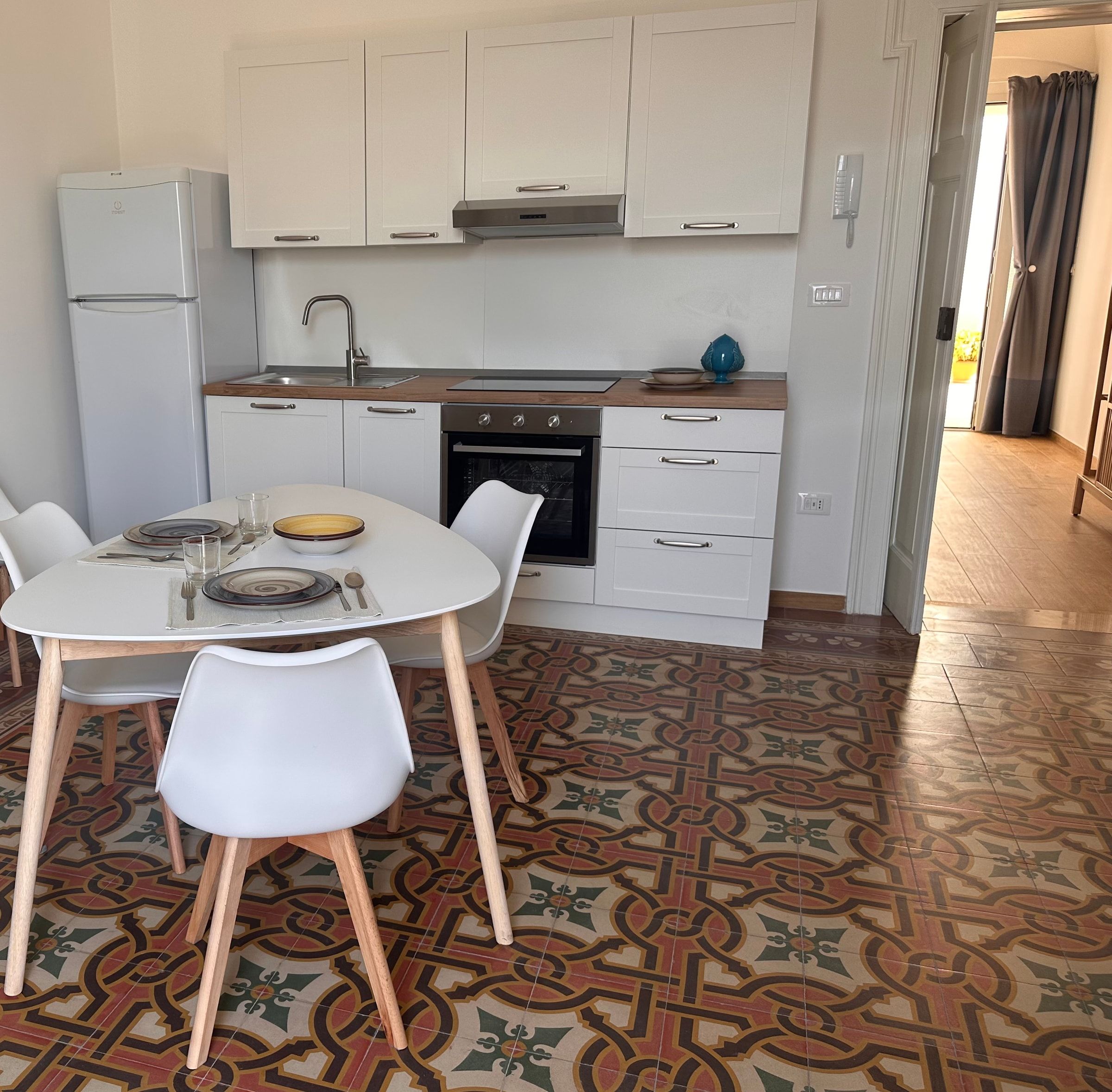 La zona pranzo con il tavolo apparecchiato e l’angolo cottura bianco, vista dal soggiorno